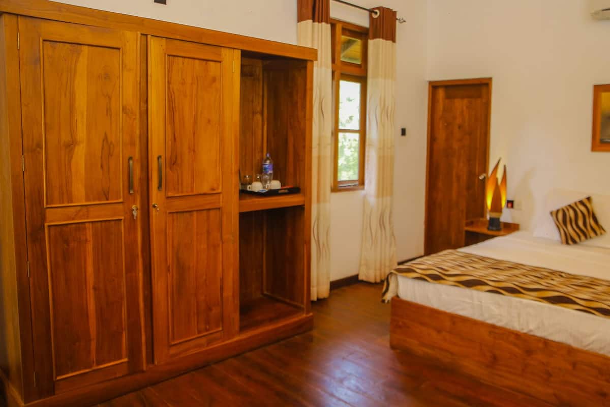 A bedroom with a wooden wardrobe, a bed with patterned bedding, a nightstand with a lamp, and a painting on the wall.