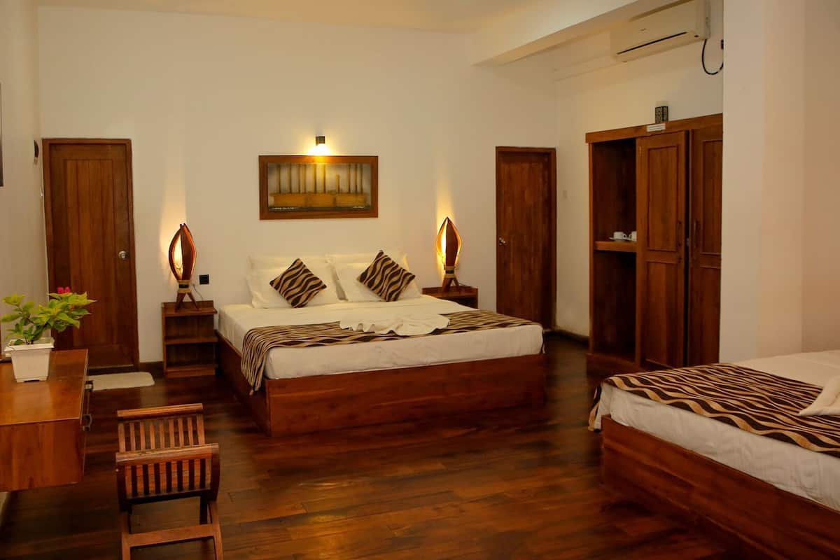 A hotel room with a large bed, a smaller bed, a desk with a chair, a wardrobe, and a mirror.