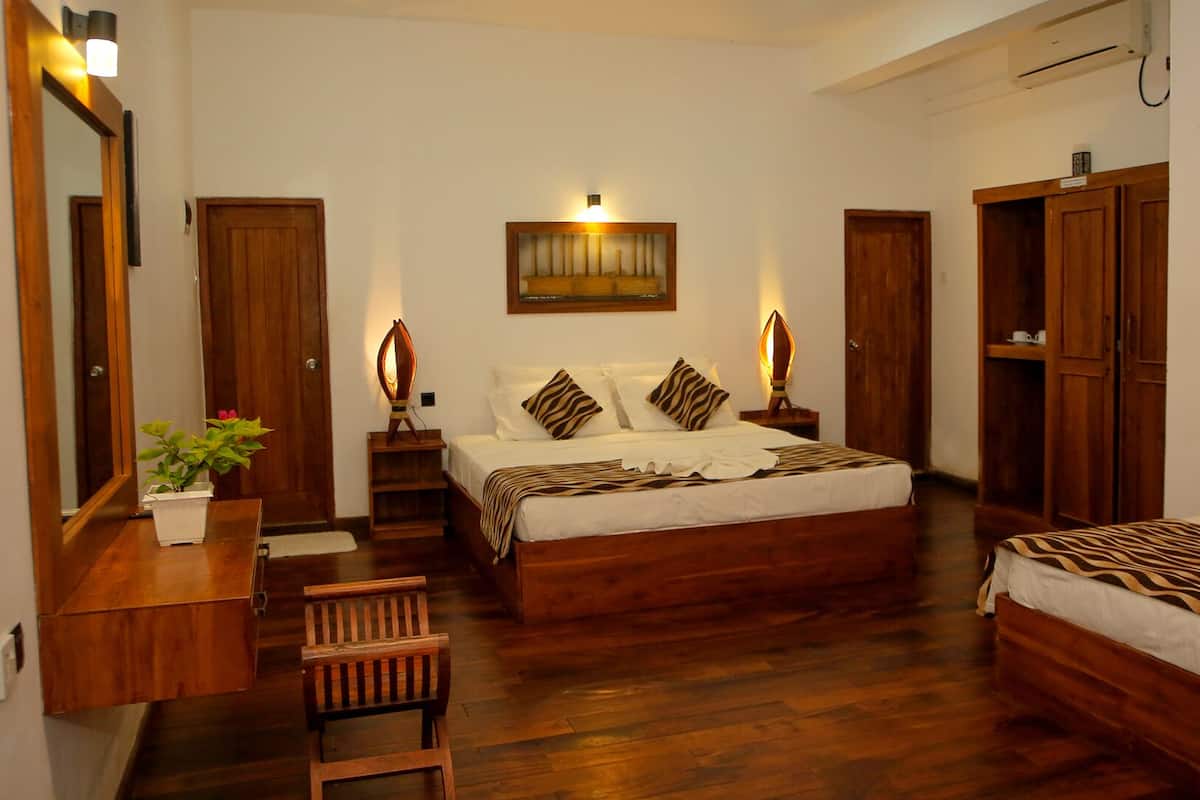 A hotel room with a large bed, a smaller bed, a desk with a chair, a wardrobe, and a mirror.