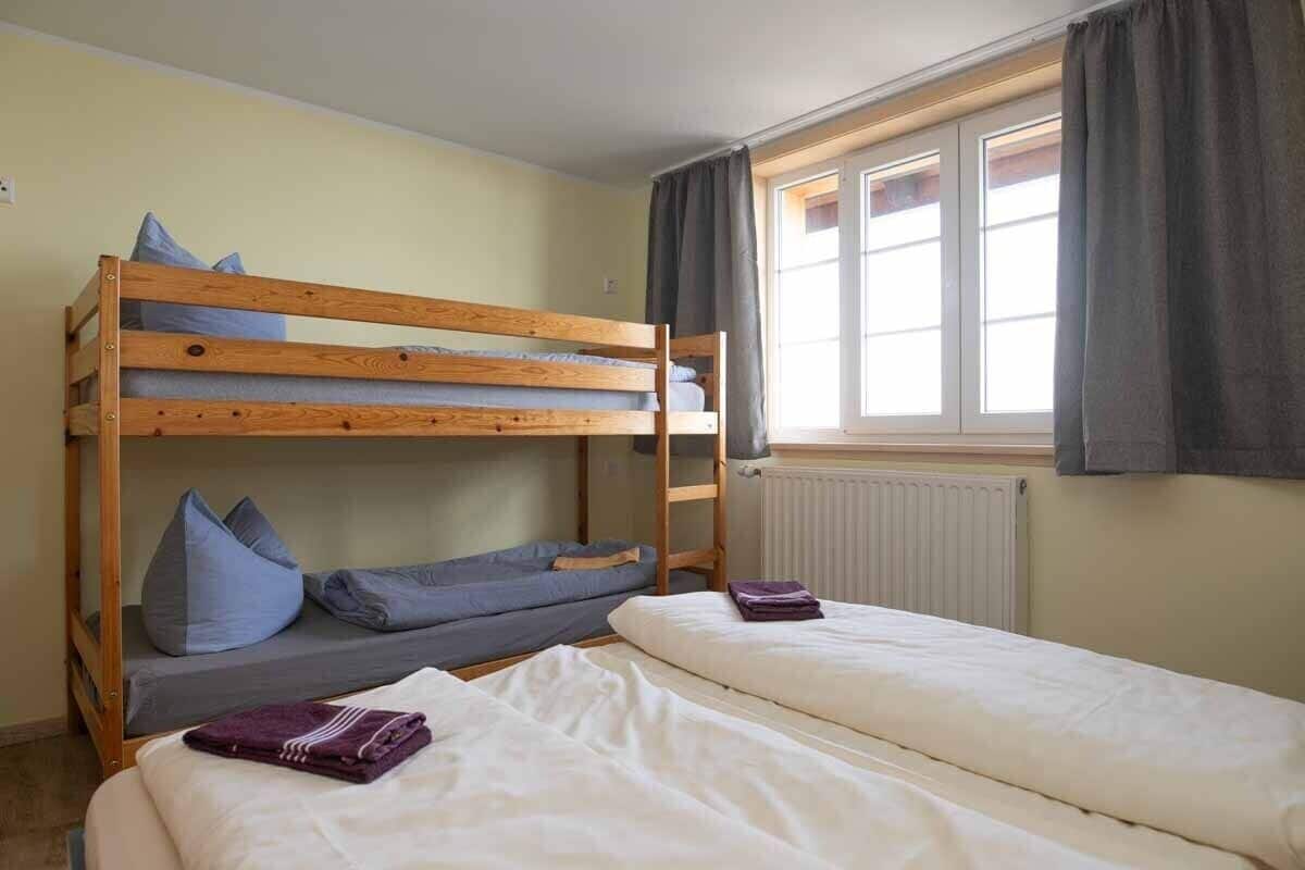 A bunk bed room with a window, a radiator, and a bed with a purple blanket.
