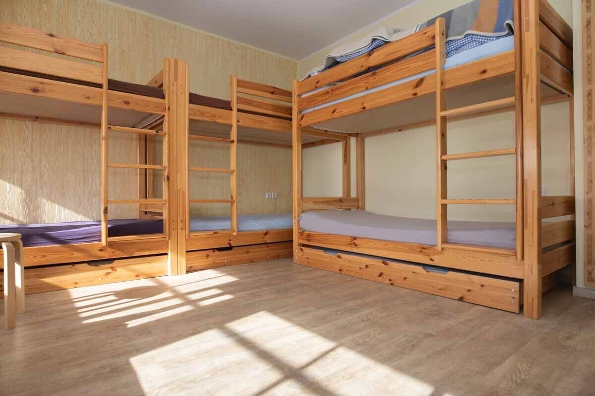 A room with three bunk beds, wooden flooring, and a window allowing natural light.