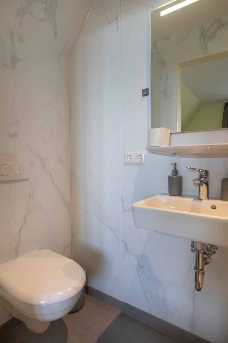 Un baño con inodoro blanco, lavamanos con espejo y paredes de mármol.