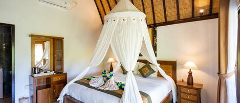 Ein Schlafzimmer mit Baldachinbett, Holzmöbeln, einem Spiegel, Nachttischlampen und einem Deckenventilator.