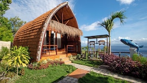 Una casa de madera con techo de paja, terraza de madera y vista al mar.
