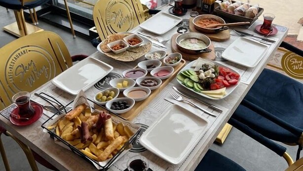 Mesa de jantar com diversos pratos e bebidas, em um ambiente com vista para a cidade.