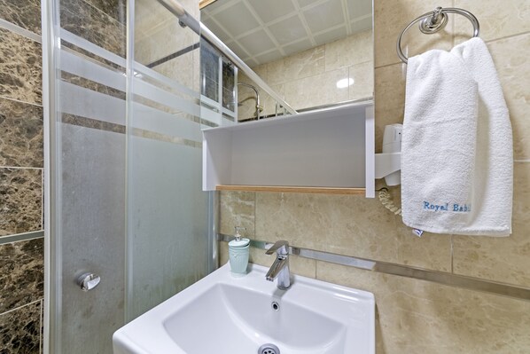 Un baño con un lavabo blanco, cabina de ducha de vidrio y un perchero con una toalla que dice "Royal Baby".