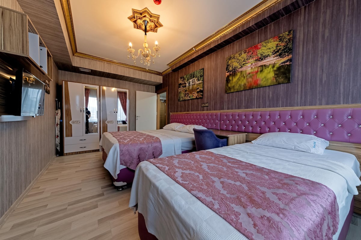 Habitación de hotel con dos camas, un ventanal grande, un candelabro y un cuadro en la pared.
