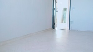 Una habitación con piso de madera clara, una puerta blanca y un enchufe visible en la pared.