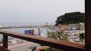 Vista costera con un puerto deportivo, un faro rojo y un edificio con grúas de construcción.
