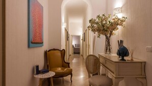 A hallway with a yellow armchair, a small round table, a wicker chair, a dresser, and a vase with flowers. - PalazzinApulia (Fasano)