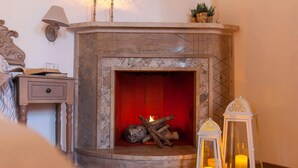 A fireplace with logs, a nightstand with a lamp, and two lit lanterns. - PalazzinApulia (Fasano)