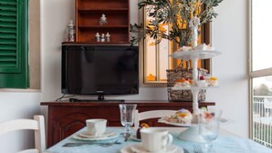 A dining area with a table set for two, a television on a stand, and a window with a view of greenery. - PalazzinApulia (Fasano)