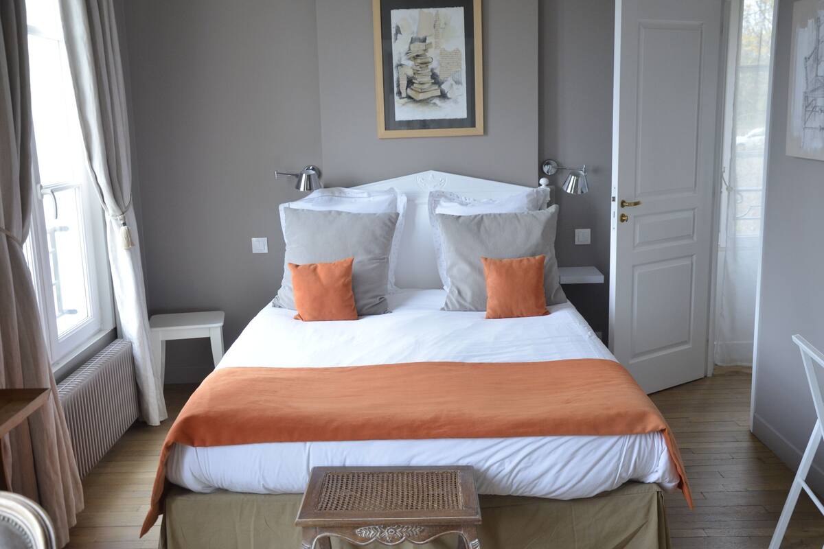 A bedroom with a large bed, two bedside tables, a radiator, and a window with curtains.