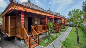 A traditional wooden building with a tiled roof, a porch with wooden railings, and a small garden area with palm trees.