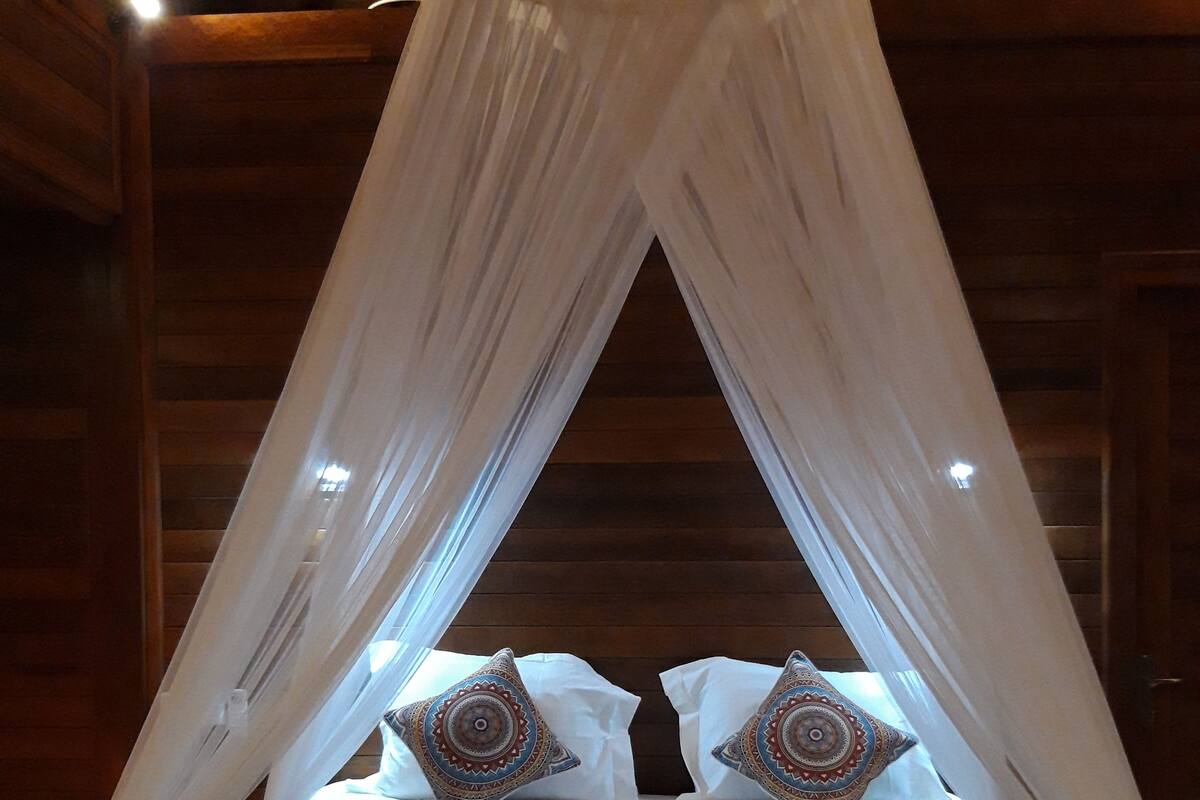 Una cama con dosel, almohadas y una colcha a rayas.
