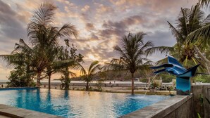 A swimming pool surrounded by palm trees and a sunset.