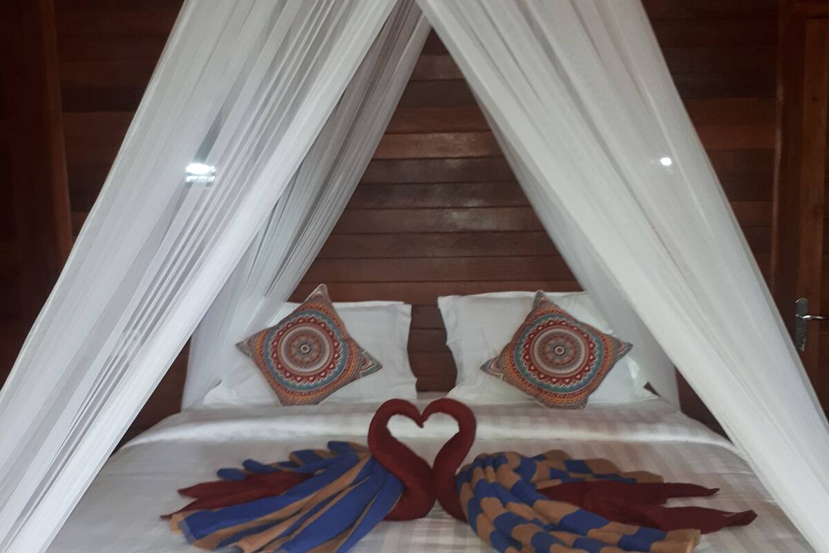 Una cama con dosel, dos toallas con forma de corazón y almohadas estampadas.