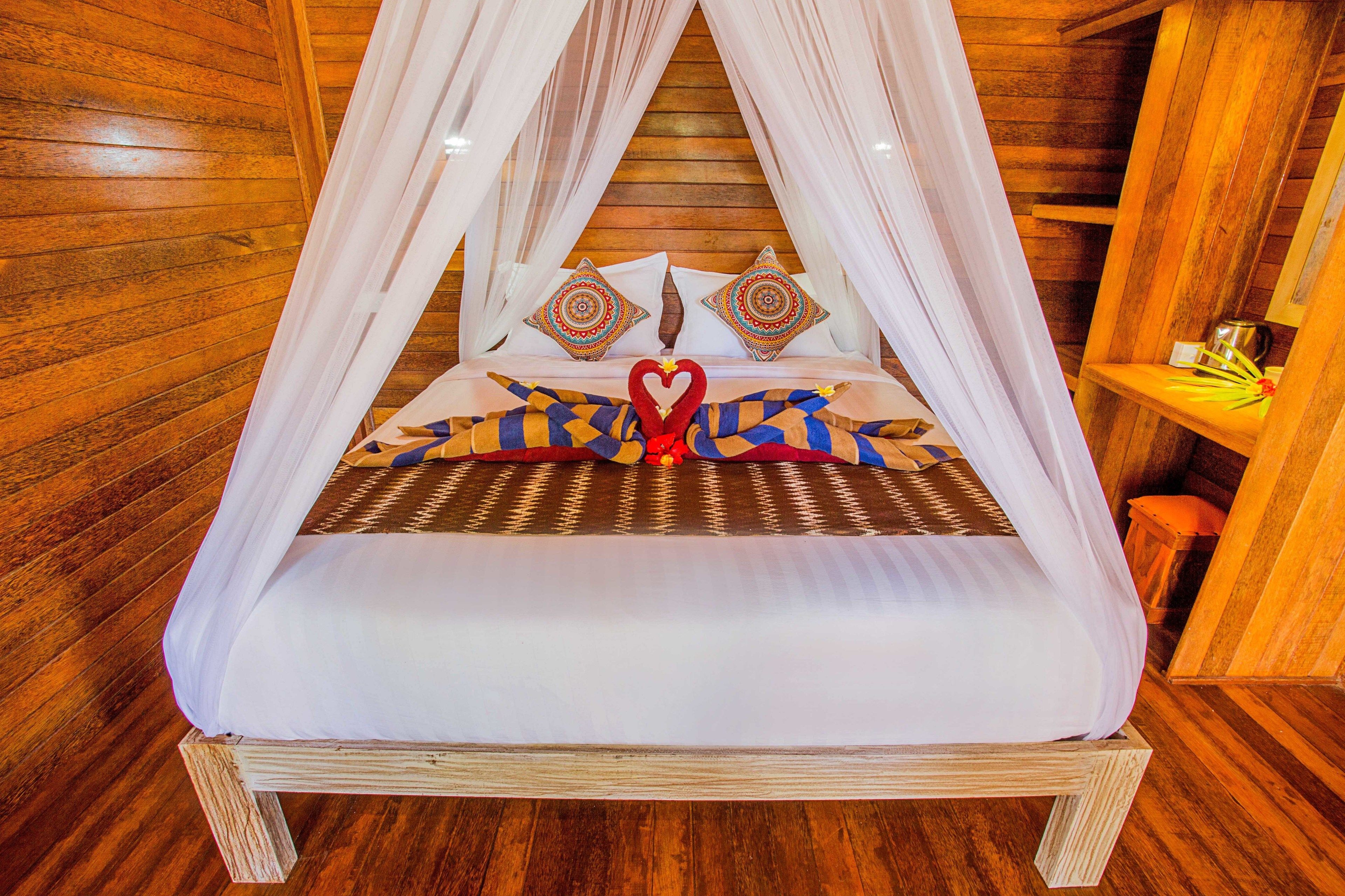 Una cama con dosel, almohadas estampadas y un adorno con forma de corazón en la colcha.