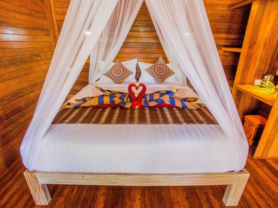 Una cama con dosel, almohadas estampadas y un adorno con forma de corazón en la colcha.
