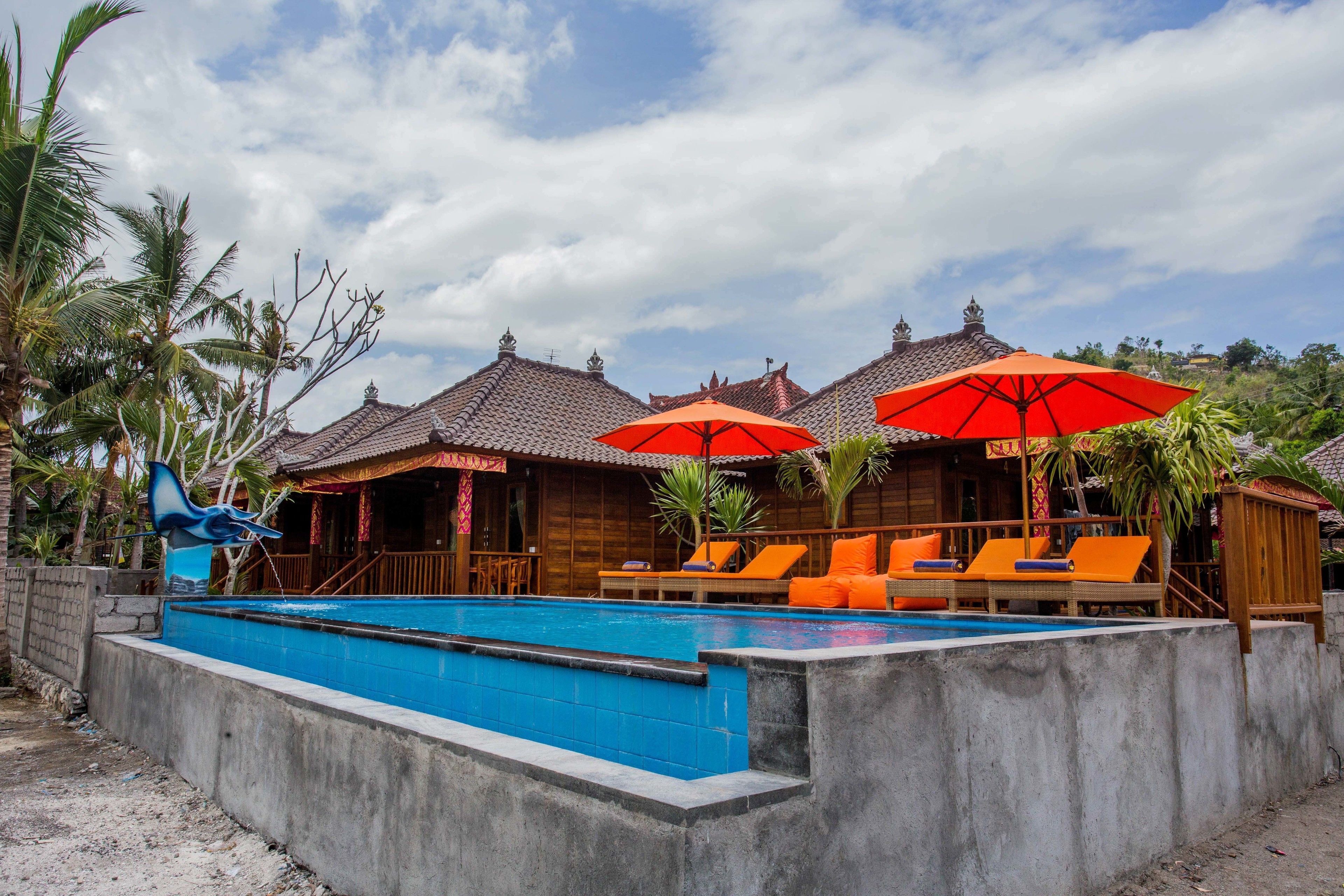 A swimming pool with lounge chairs and umbrellas, surrounded by wooden buildings with tiled roofs.