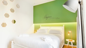 A neatly made bed with white linens, a green accent wall with a quote, and a small table with a lamp. - Italianway   - Passeroni 2 (Milan)