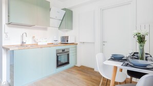 A modern kitchen with light blue cabinets, a built-in oven, and a dining area with white chairs and a table set for two. - Italianway   - Passeroni 2 (Milan)