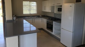 A modern kitchen with white cabinets, a black countertop, a built-in oven, a microwave, and a refrigerator. - Windmill Farm (Jagersrust)