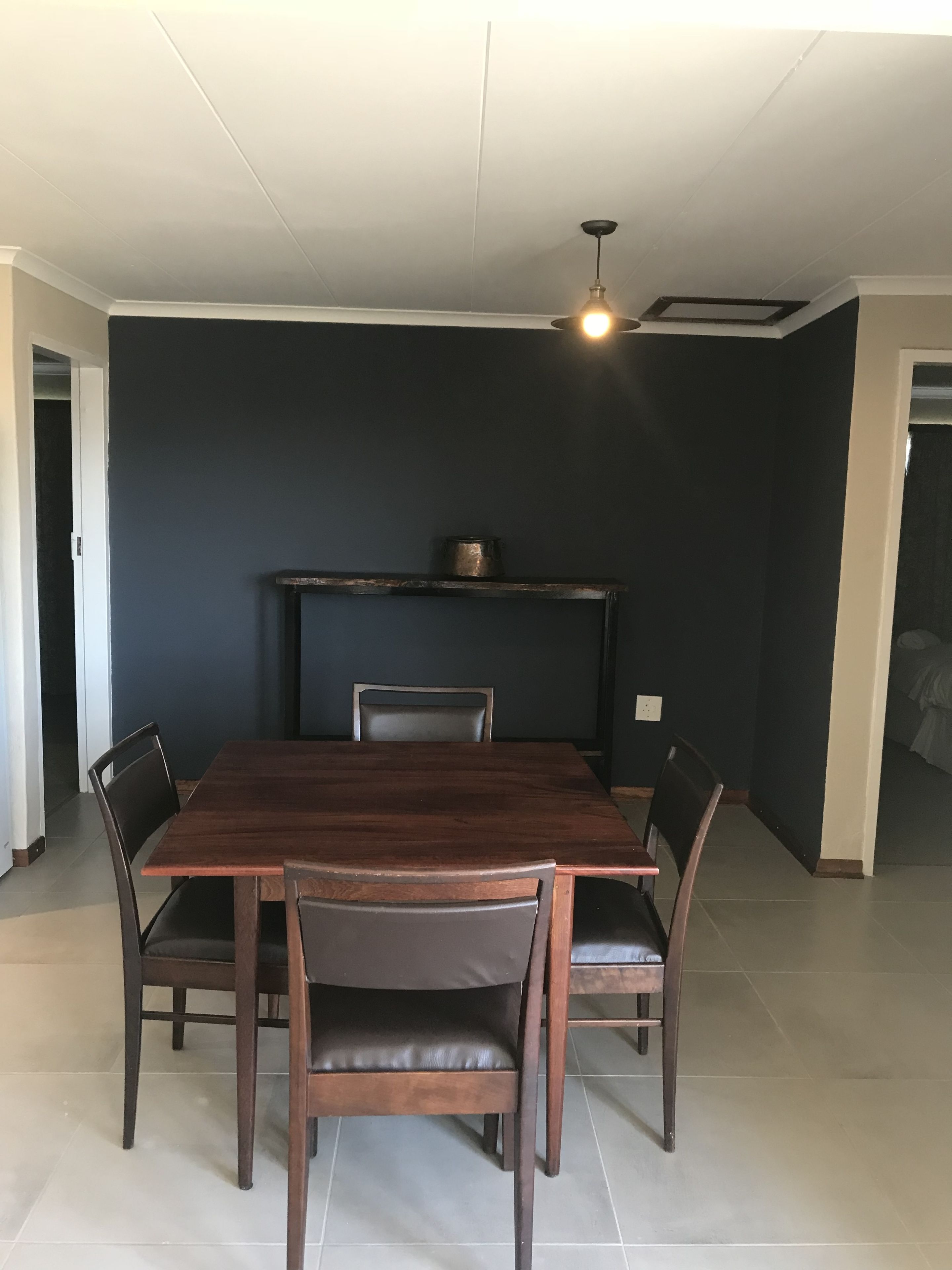 A dining area with a dark-colored wall, a wooden table, and four chairs.