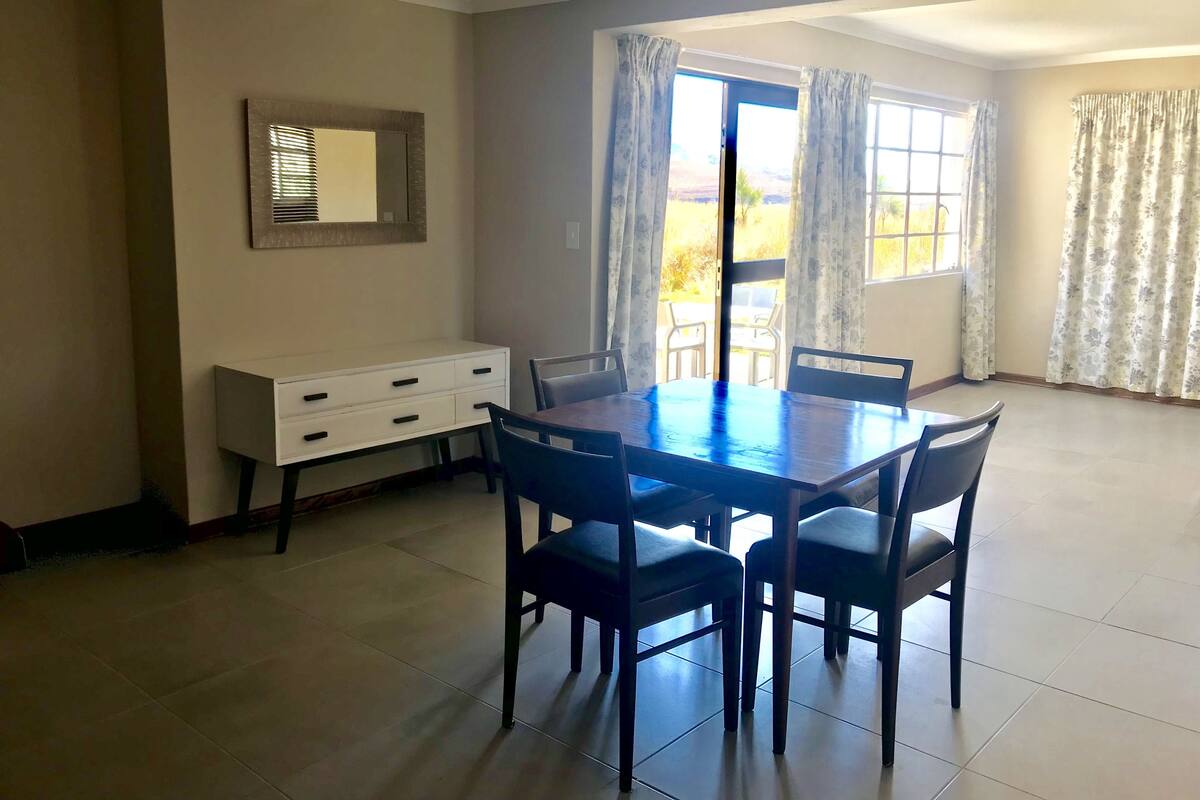 A dining area with a table and chairs, a white cabinet, and a window with curtains.