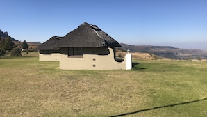 A thatched-roof building with a window and a white pillar, set against a hilly landscape. - Windmill Farm (Jagersrust)