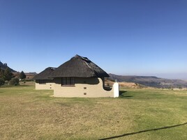 Un edificio con techo de paja, una ventana y un pilar blanco, frente a un paisaje montañoso.