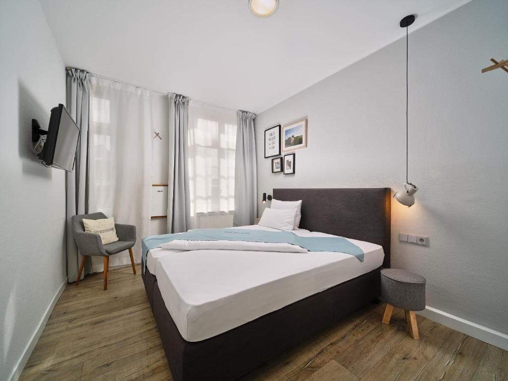 A modern bedroom with a bed, a chair, a bedside table, a TV mounted on the wall, and a window with curtains.
