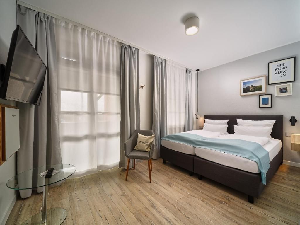 A modern hotel room with a bed, a chair, a TV, and a small table.