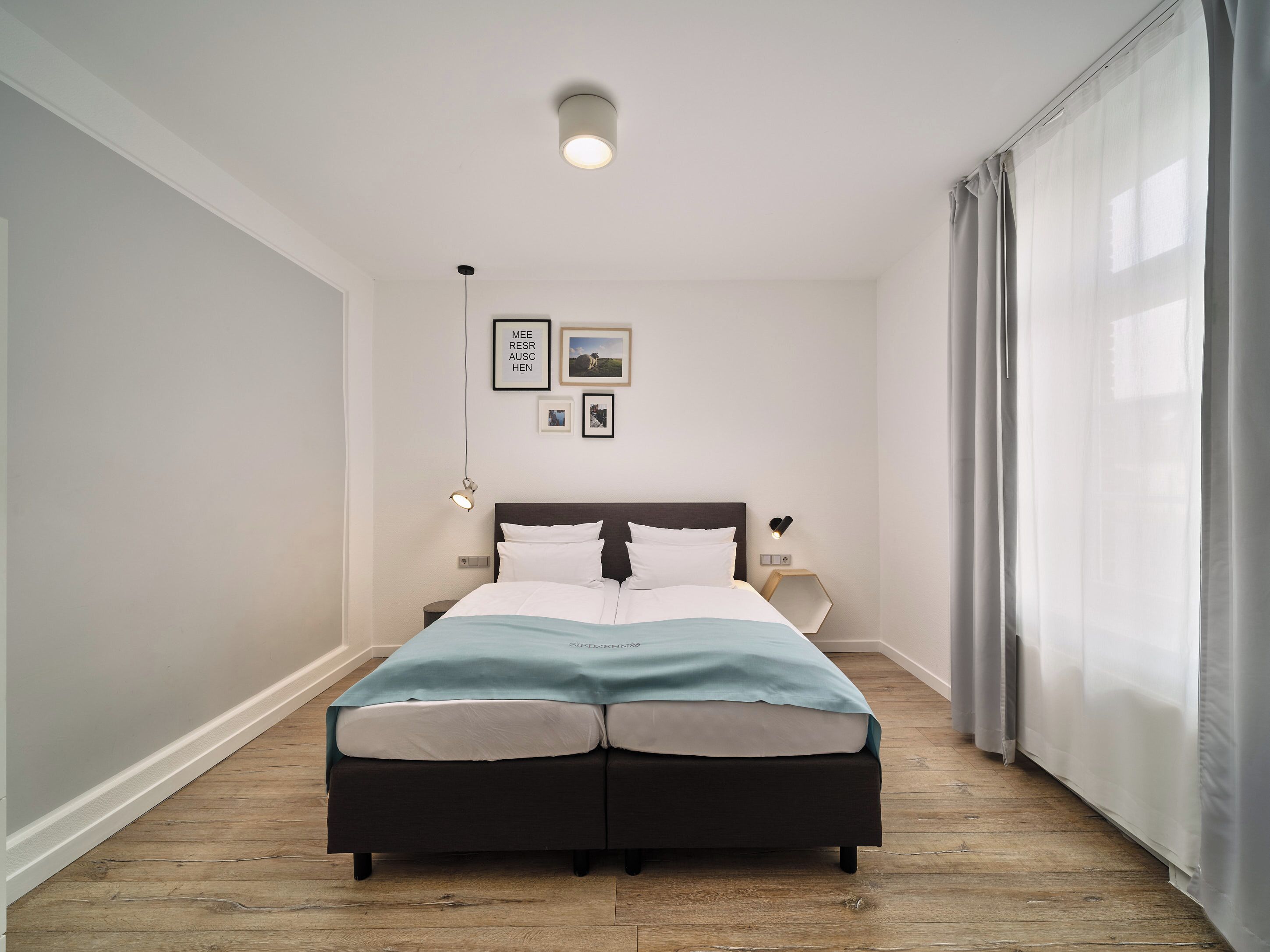 Un dormitorio con una cama en el centro, una mesita de noche con una lámpara y una lámpara de pared.