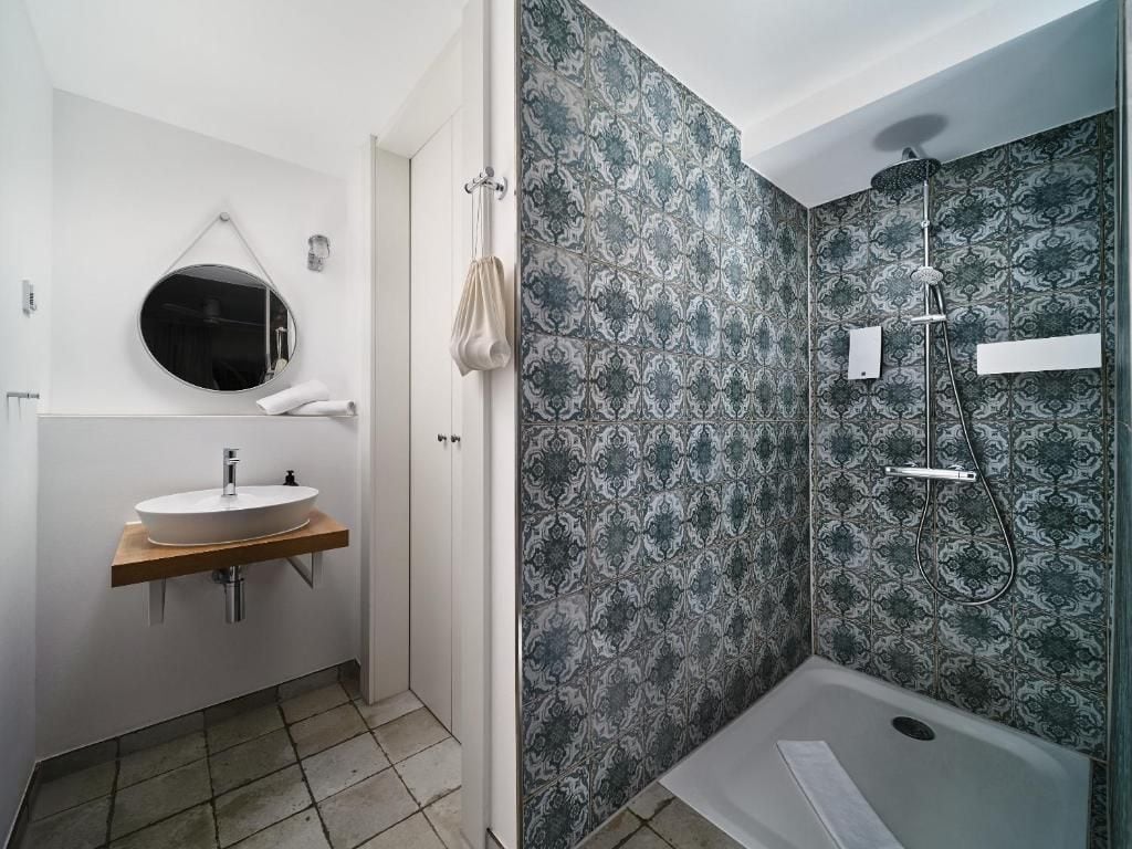Un baño con espejo redondo, lavamanos y zona de ducha.
