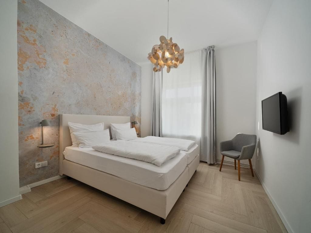 Un dormitorio moderno con una cama, una silla, un televisor y una original obra de arte en la pared.