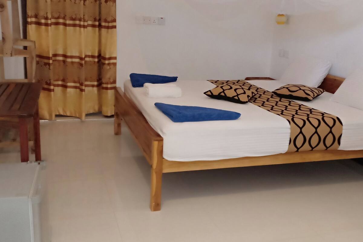 A single bed with a wooden frame, a bedside table, a chair, and a curtain.