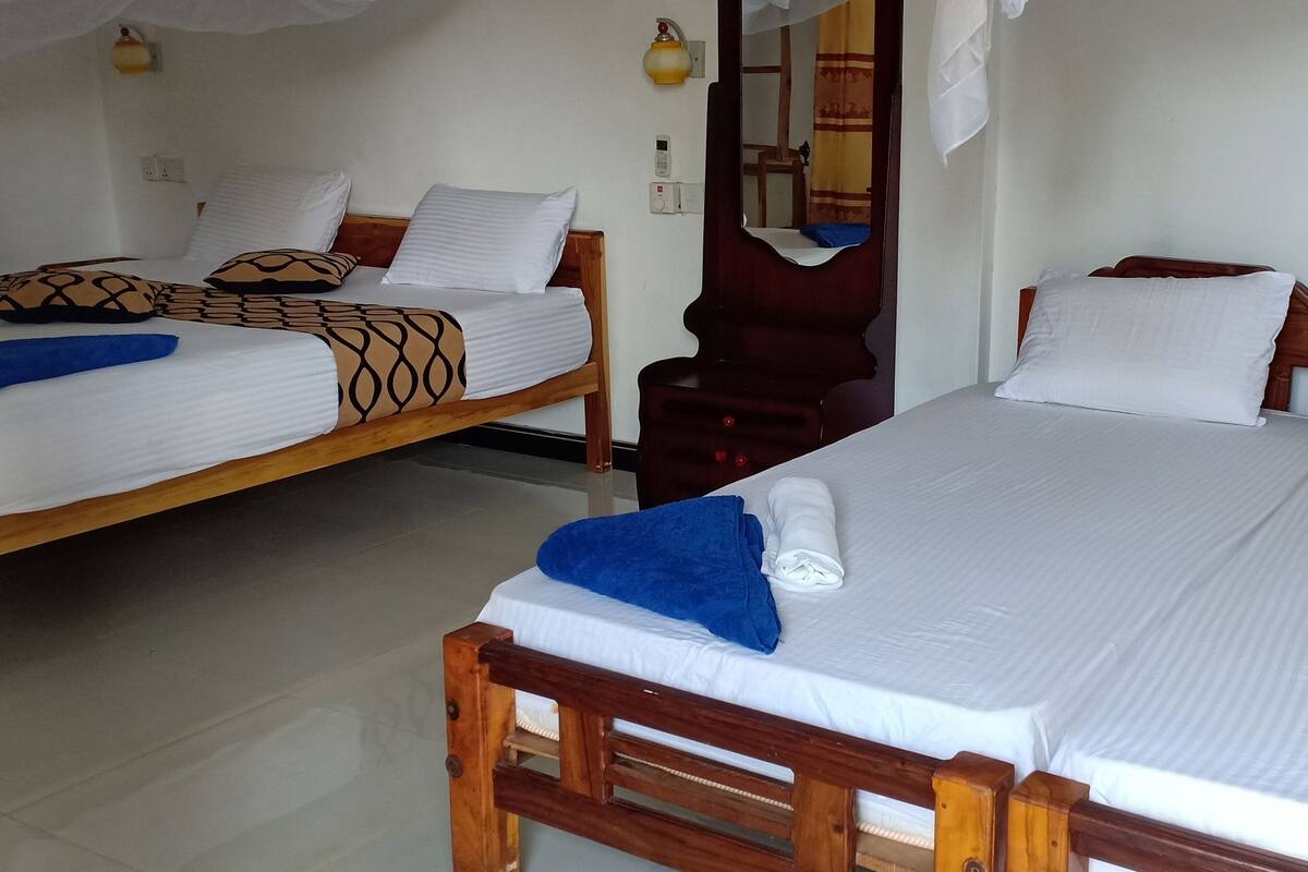 A hotel room with two beds, each with white linens and a blue towel. There are wall sockets and a mirror on the wall.