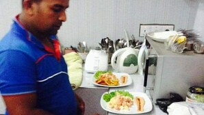Una cocina con una persona preparando alimentos, varios platos sobre la encimera y electrodomésticos.
