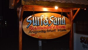Señal de madera del Restaurante y Habitaciones Surf & Sand, con información de contacto.