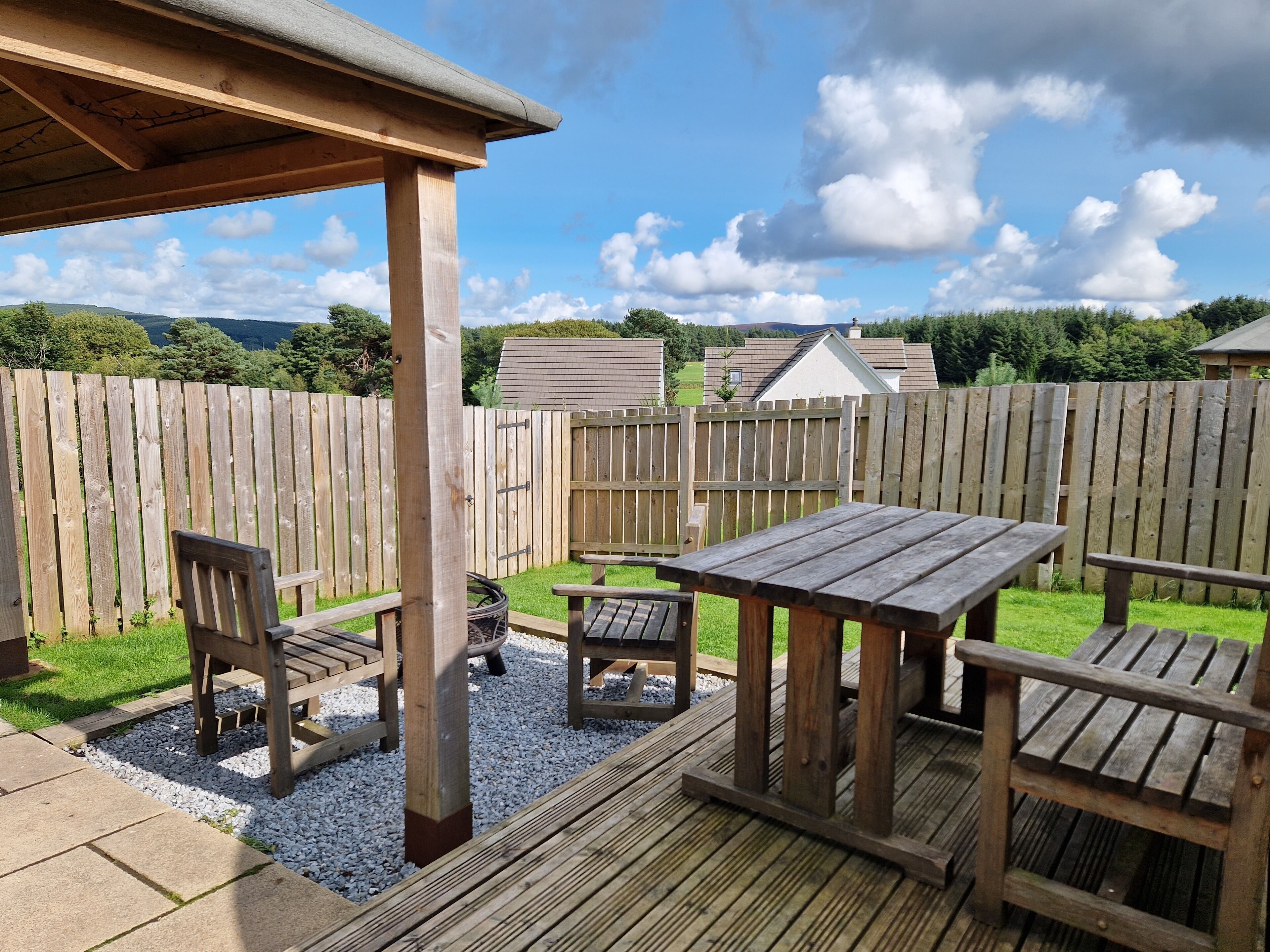 A wooden deck with a pergola, picnic table, and chairs.