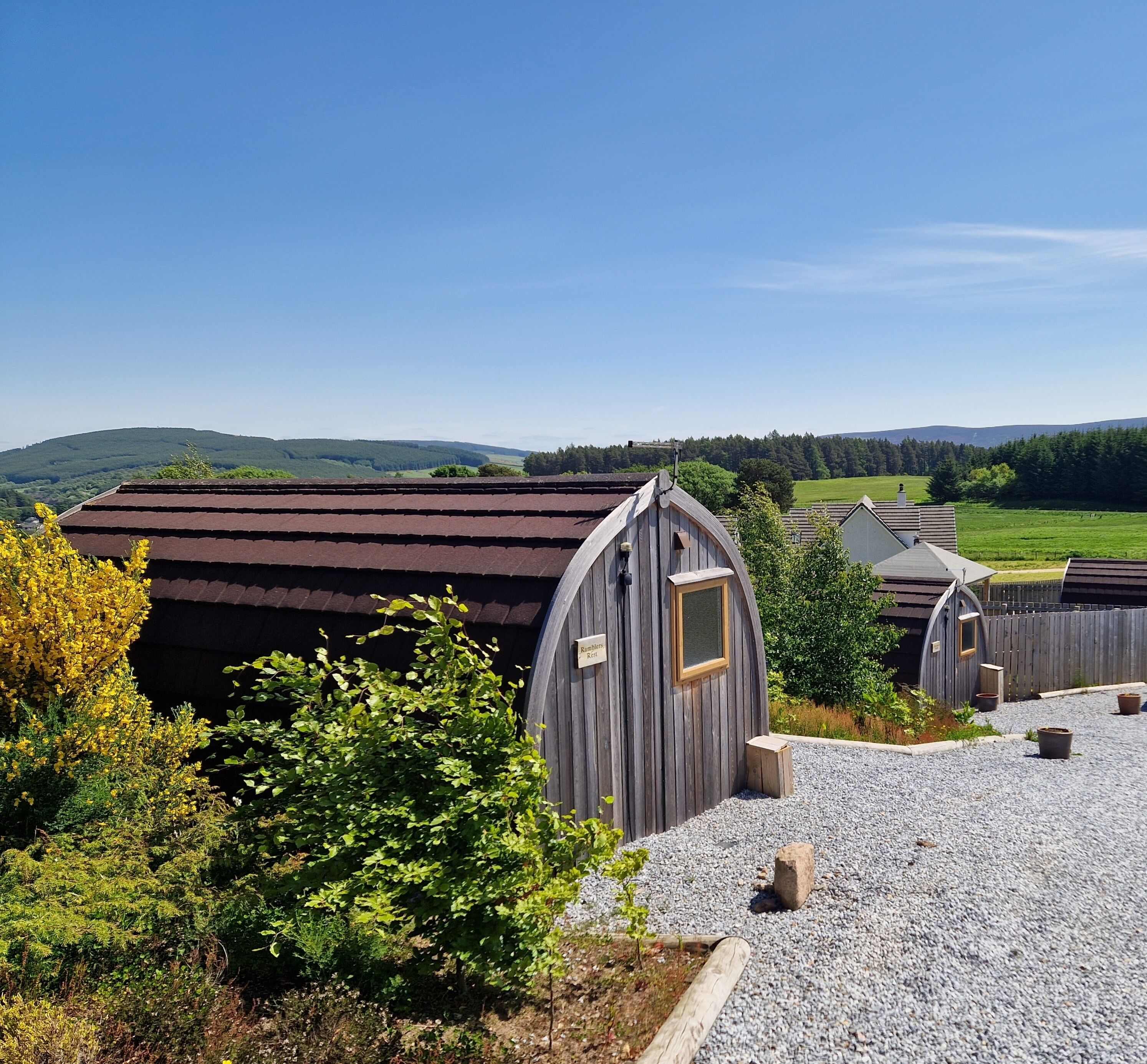 A rural setting with wooden buildings, gravel paths, and a clear view of distant hills.