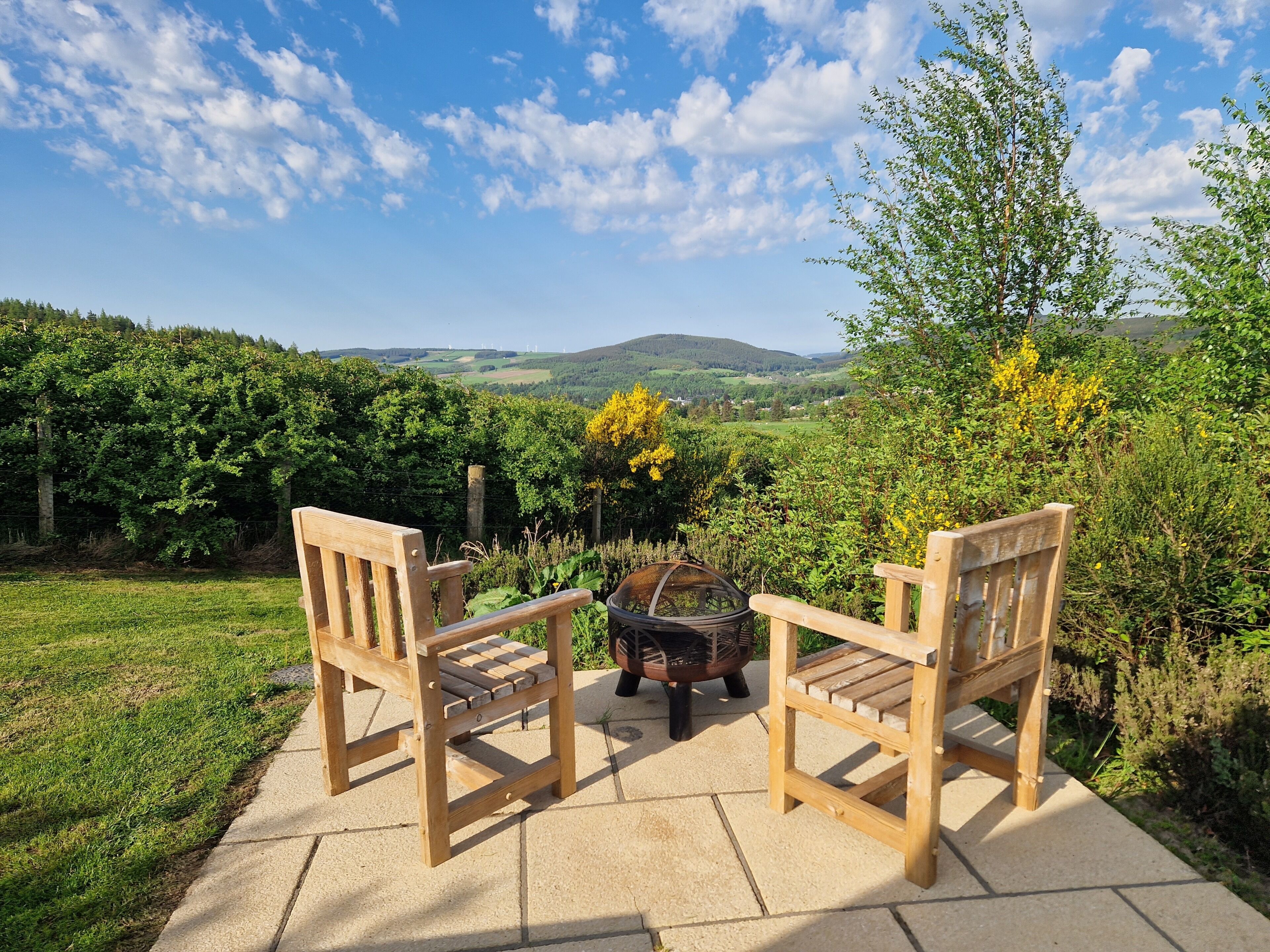 Deux chaises en bois sur une terrasse, avec vue sur un paysage verdoyant et des collines.