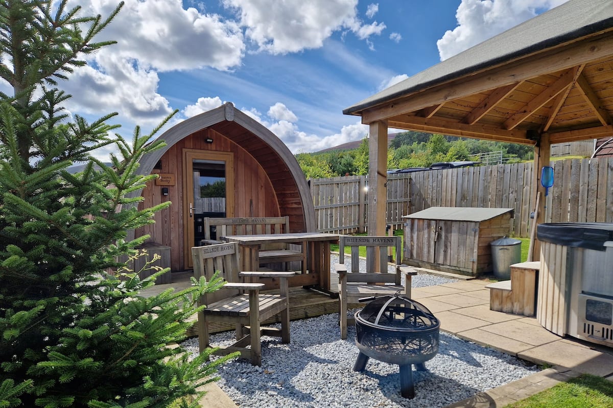 A rustic outdoor seating area with wooden furniture, a fire pit, and a covered patio.