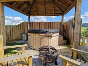 A wooden outdoor seating area with a hot tub, a fire pit, and a wooden deck. - Hillside Havens (Keith)