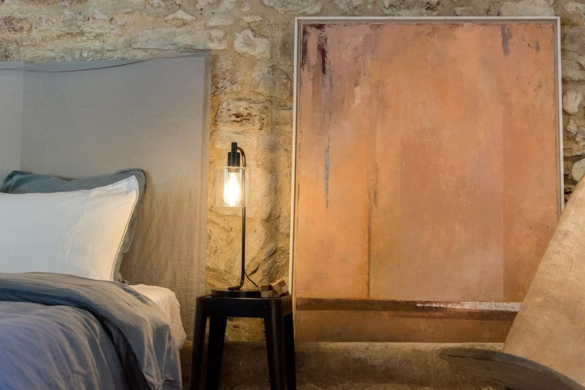 Een slaapkamer met een stenen muur, een bed met een wit hoofdeinde en een houten deur.