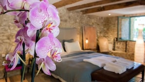 A bedroom with a stone wall, a bed with white linens, and a bouquet of pink orchids. - La Belugue (Beaumont-de-Pertuis)