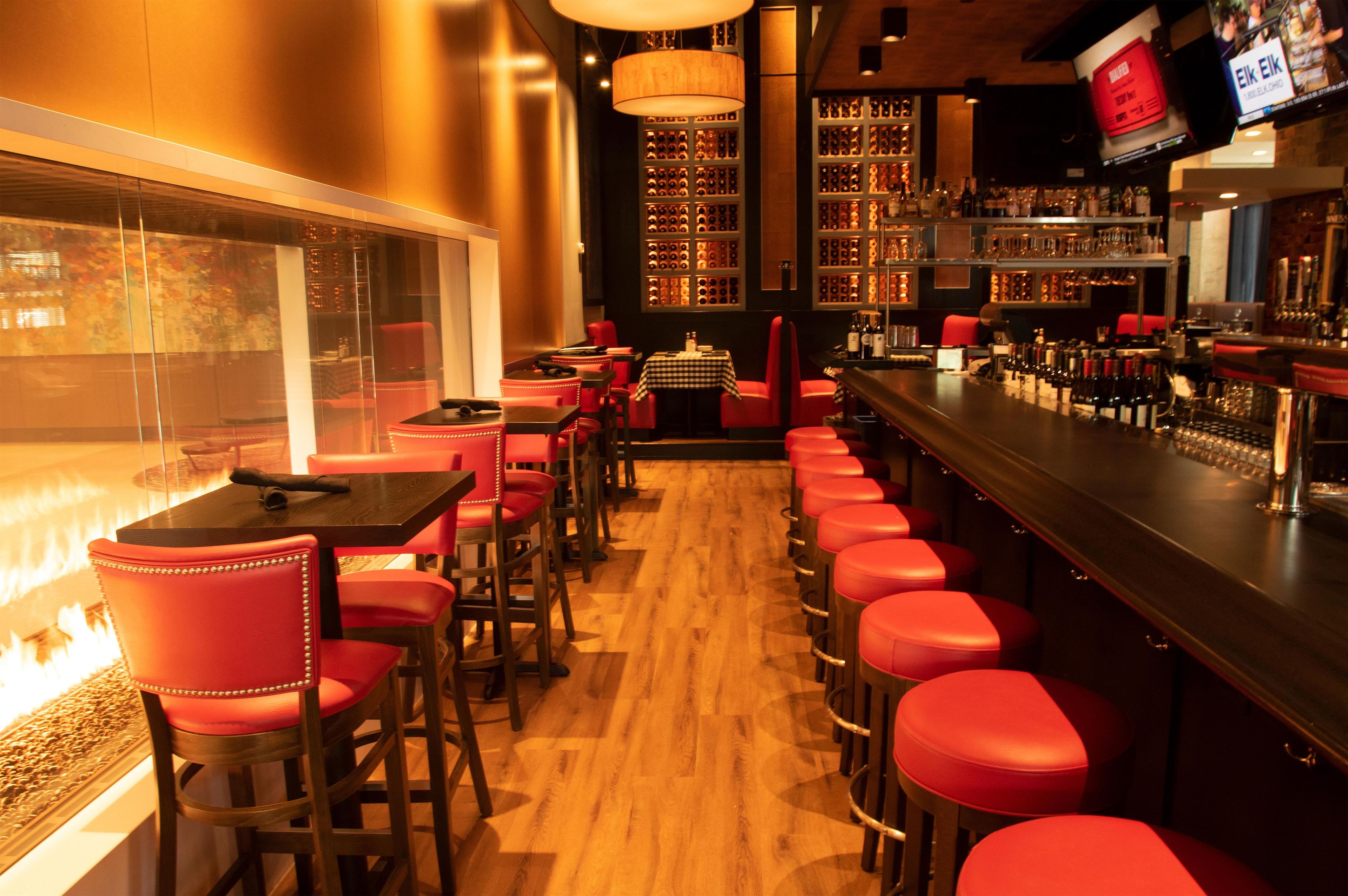 Un espace bar avec des tabourets rouges, un plancher en bois et un mur recouvert de bouteilles de vin.