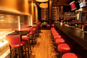 Un espace bar avec des tabourets rouges, un plancher en bois et un mur recouvert de bouteilles de vin.