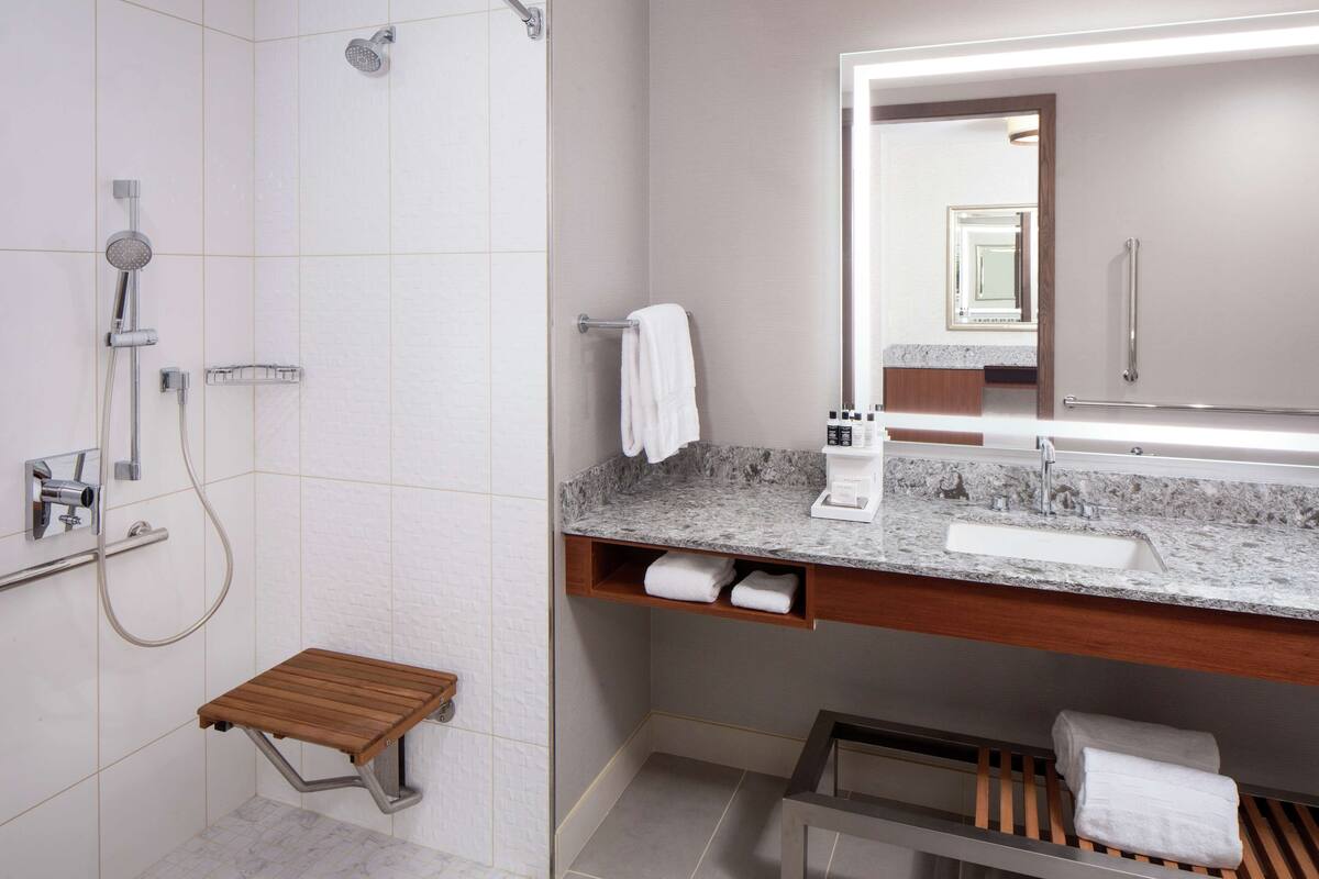 A modern bathroom with a shower, a vanity with a sink, a mirror, and a wooden stool.